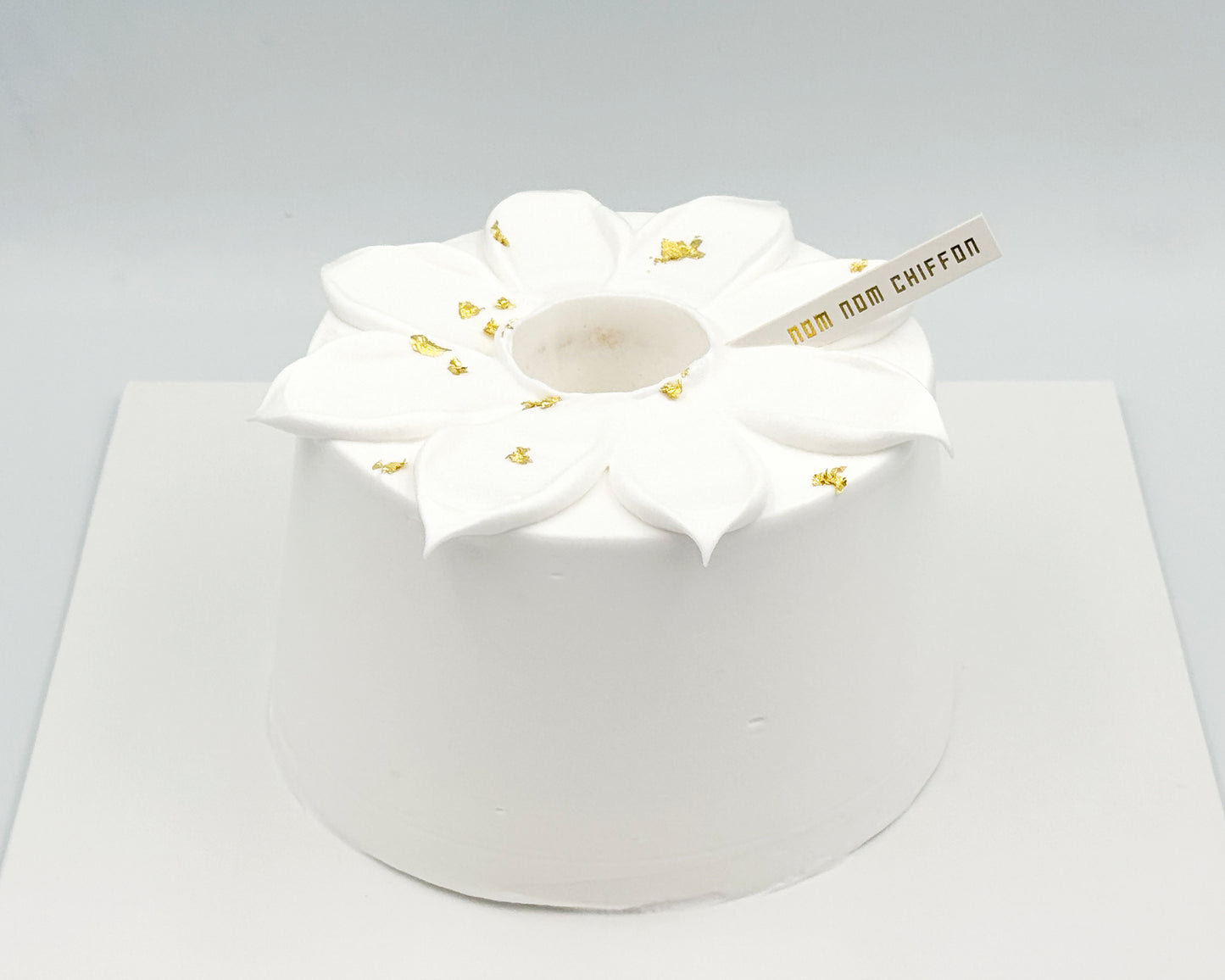 White frosted cake with flower petal piping and gold leaf accents on a gray background