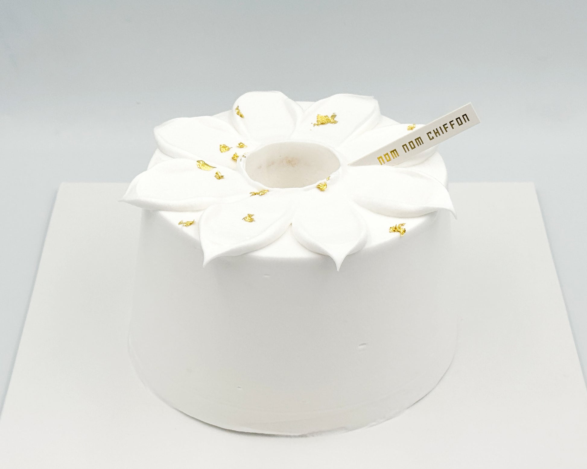 White frosted cake with flower petal piping and gold leaf accents on a gray background