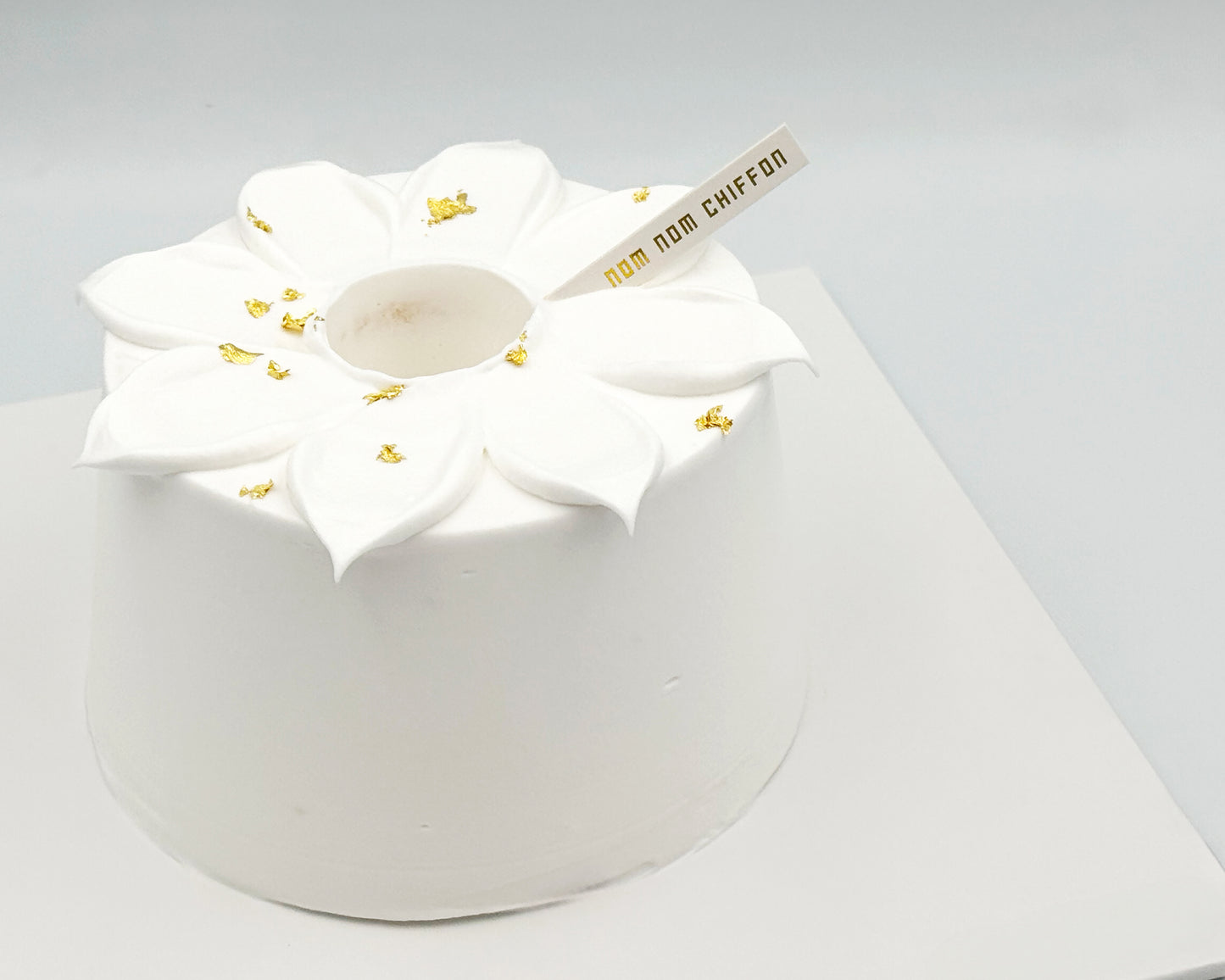 White chiffon cake with floral petals, gold leaf, on a white background