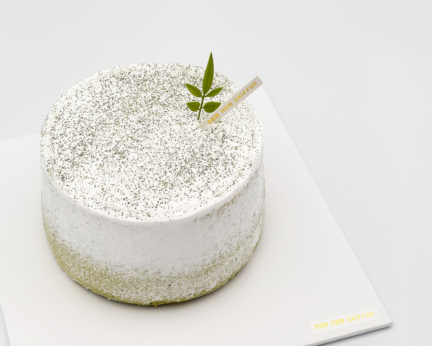 Matcha green tea chiffon cake with a leaf decoration, with light crumb coat frosting, on a white background, side view