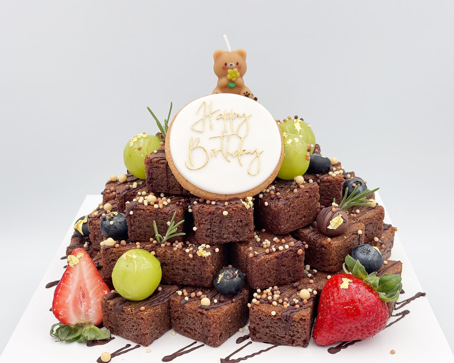 Brownie stacked cake with berries and a 'Happy Birthday' candle on a white background