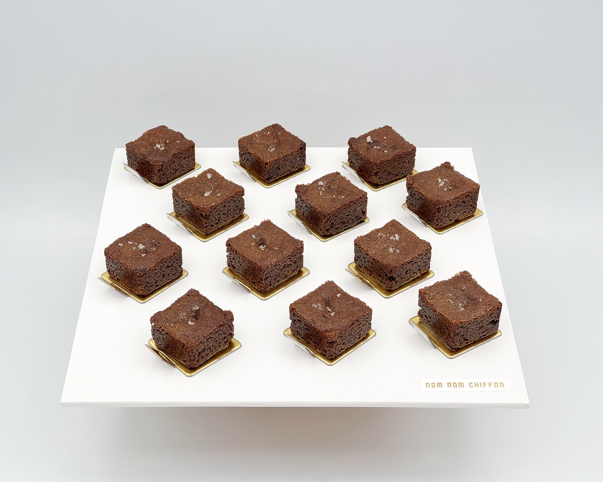 Brownies on gold square plates arranged in a grid on a white background