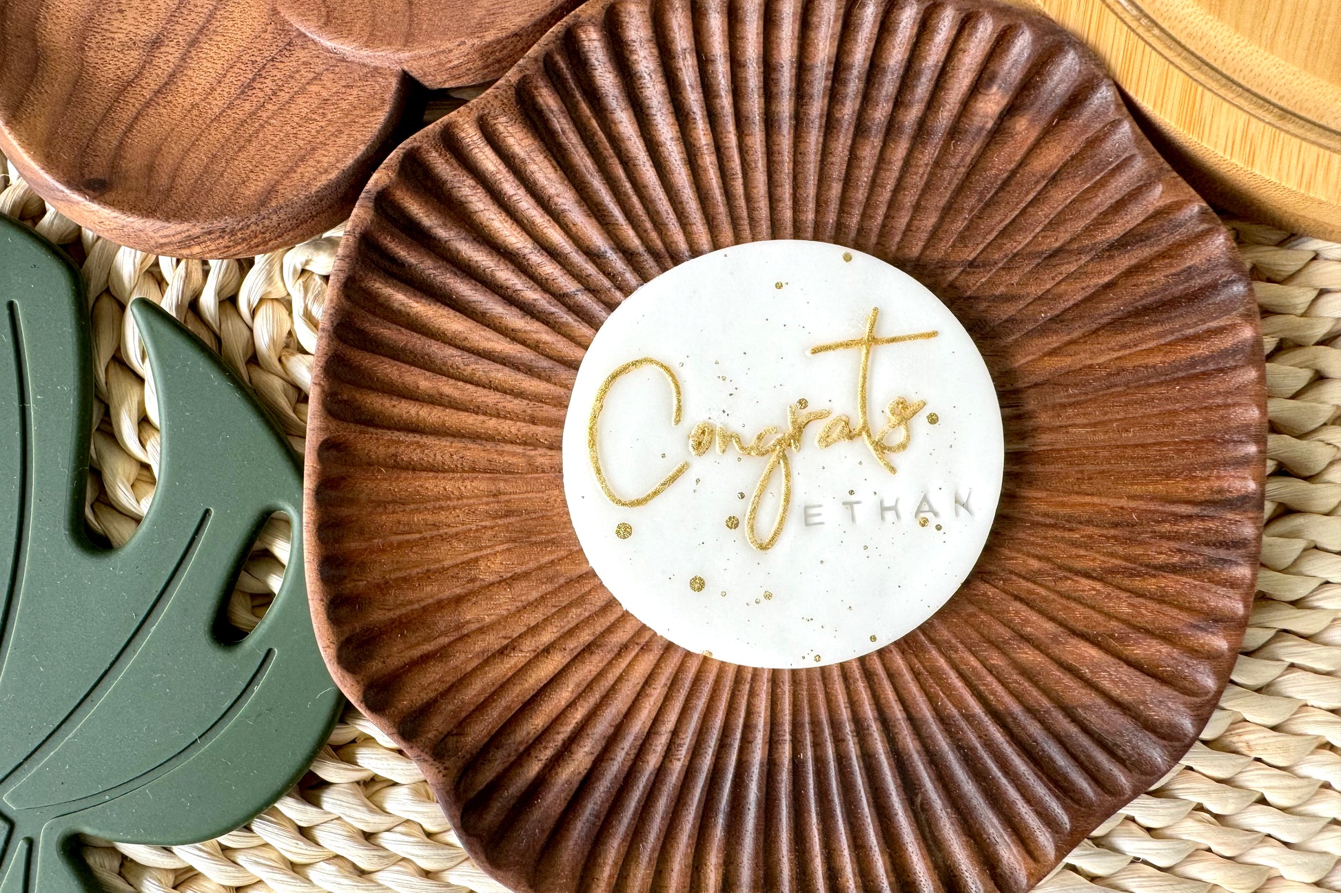 Wooden coaster with a white label reading 'Congrats Ethan' on a woven surface.