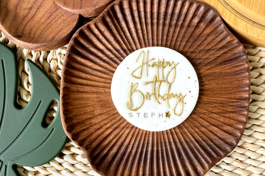 Wooden coaster with cake topper 'Happy Birthday Steph' label on a woven surface
