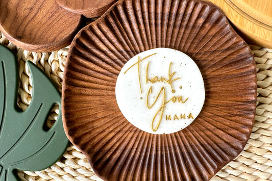 Wooden coaster with cake topper 'Thank You Mama' message on a woven surface
