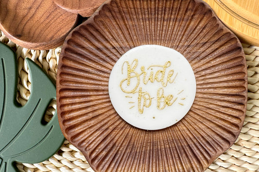 Decorative cake topper with 'Bride to be' text on a woven surface