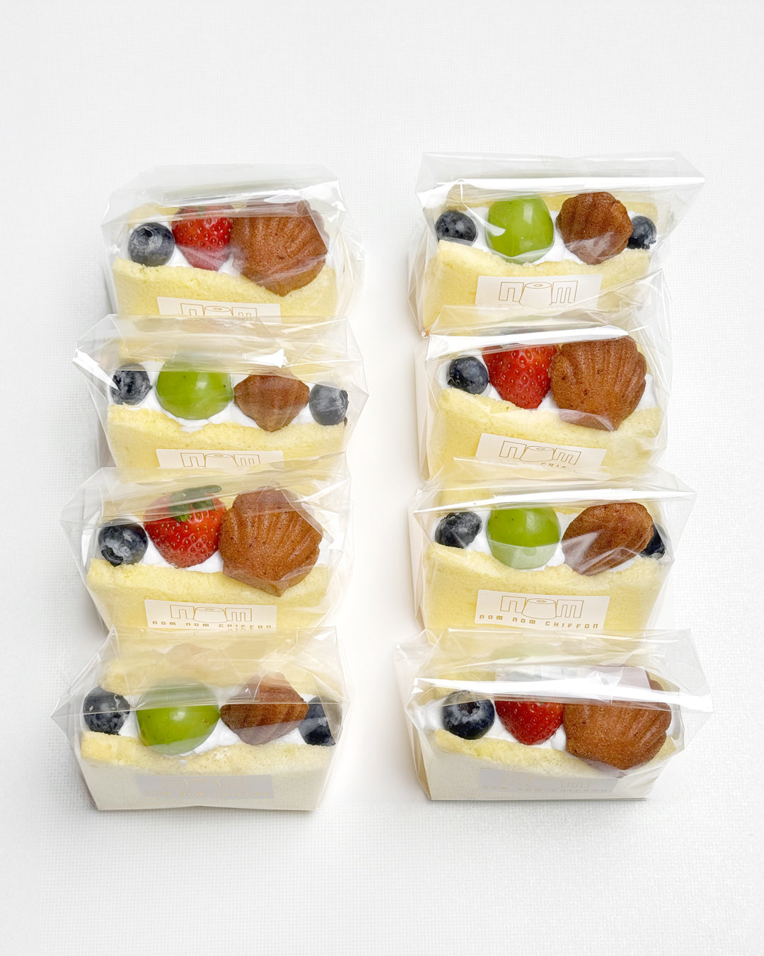 Packaged vanilla chiffon fruit sando with fruits and mini madeleines on a white background