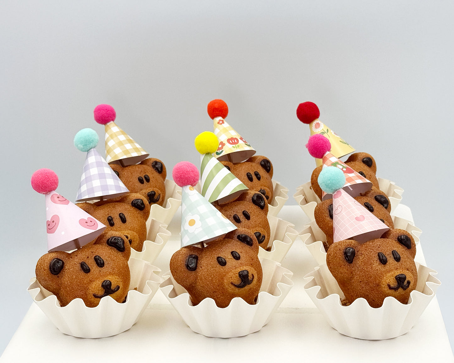 Bear-shaped madeleines wearing colorful party hats on a white background