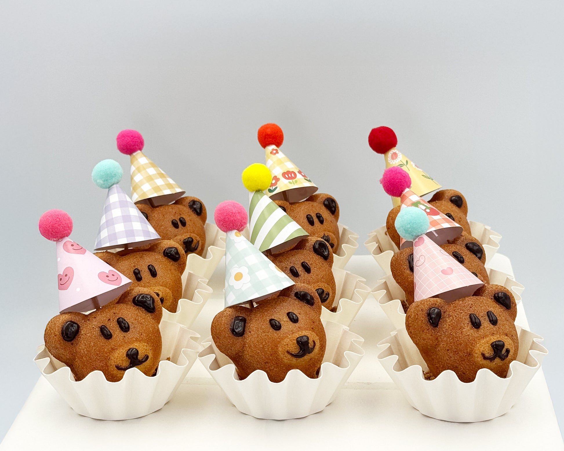 Bear-shaped madeleines wearing colorful party hats on a white background