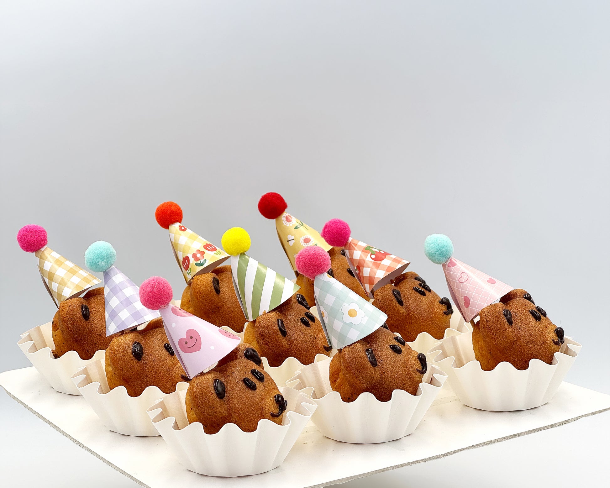 Side profile of bear madeleines with colorful party hats on a white surface.