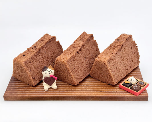 Three slices of chocolate chiffon cake on a wooden board with decorative items.