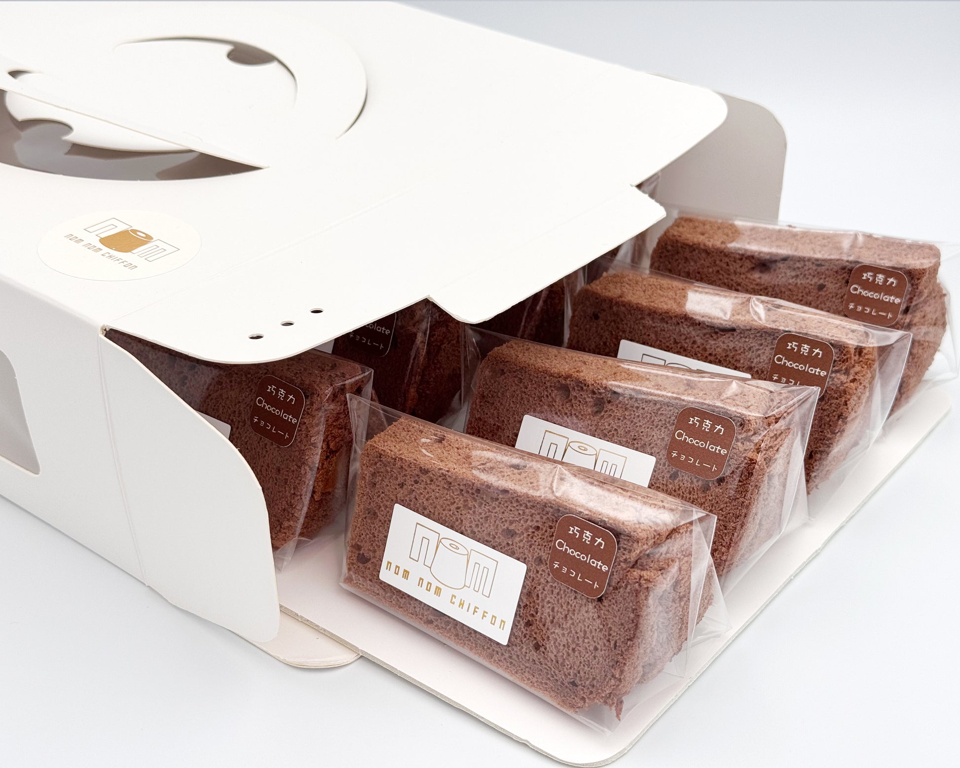 Packaged chocolate chiffon cake in clear plastic packaging with nom nom chiffon brand label on a white background.