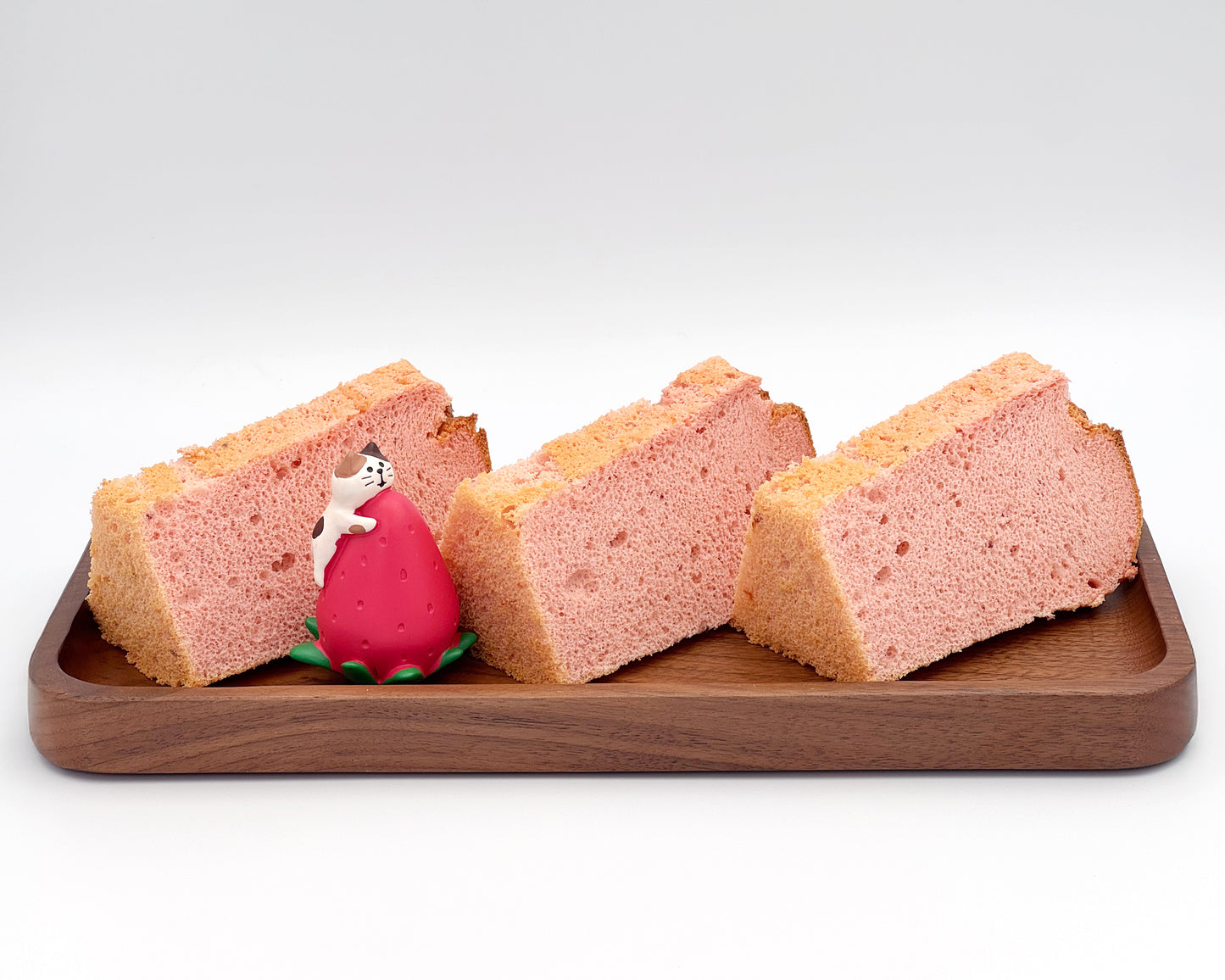 Three slices of strawberry chiffon cake on a wooden tray with a white background