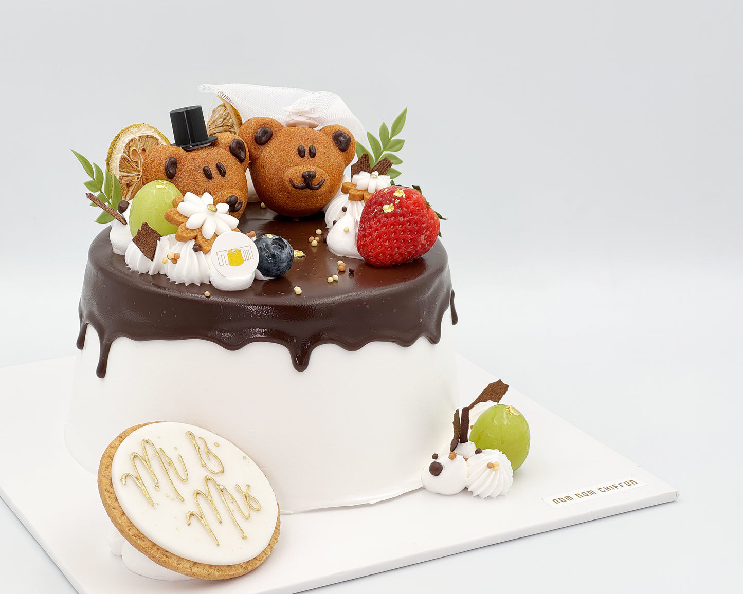 Side view of chiffon cake with teddy bear madeleines and fruit decorations on a white background