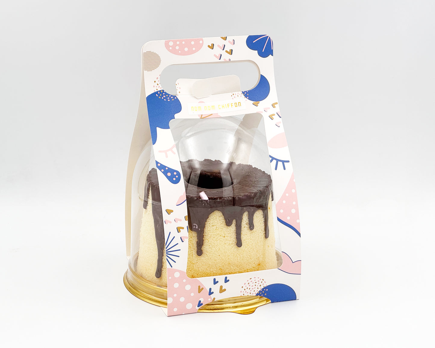 small chiffon cake with chocolate drip in a decorative packaging with colorful design on a white background