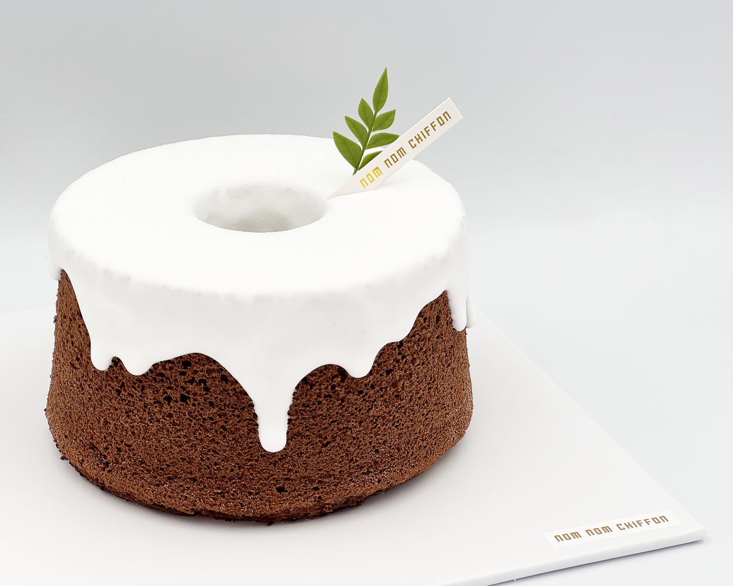 Chocolate chiffon cake with white snowcap on a gray background, featuring the brand 'Nom Nom Chiffon'.