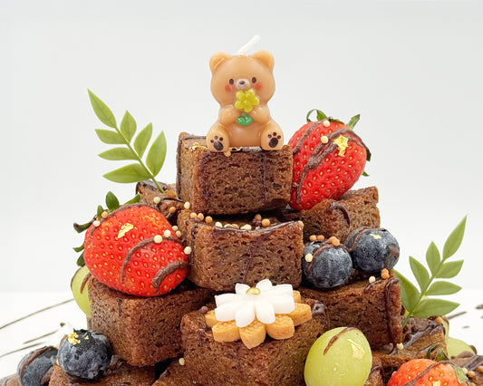 Stack of brownies with decorative elements including strawberries, blueberries, and a small bear figurine on a white background.