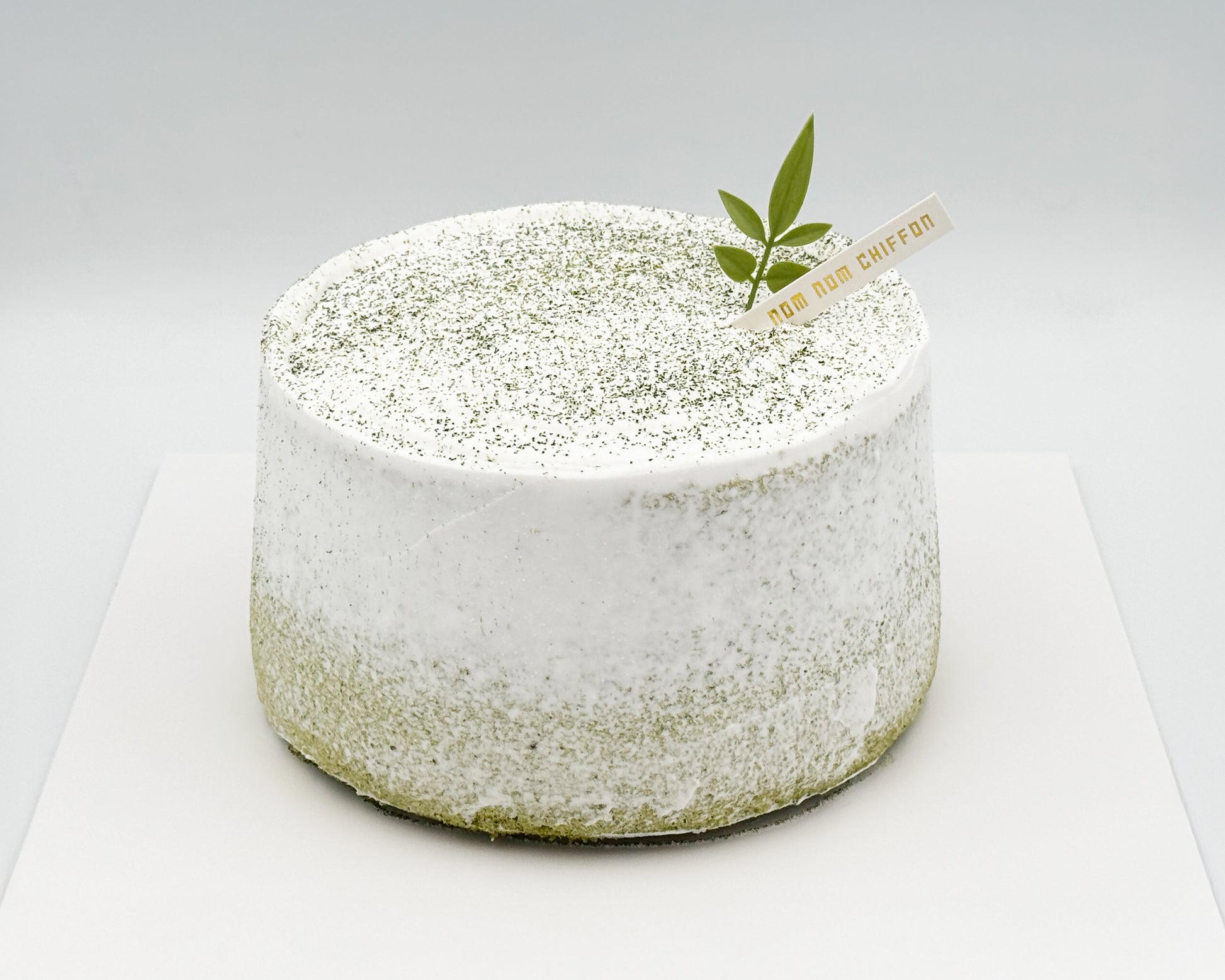 Matcha green tea chiffon cake with a leaf decoration, with light crumb coat frosting, on a white background