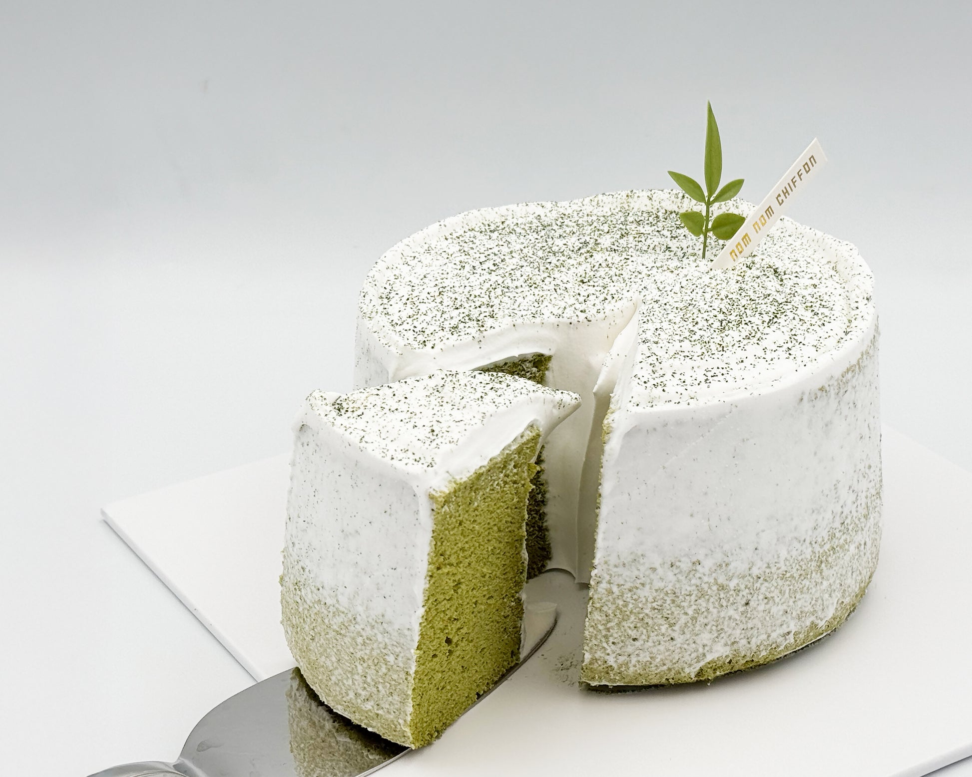 Matcha green tea chiffon cake with a leaf decoration, with light crumb coat frosting, on a white background, sliced