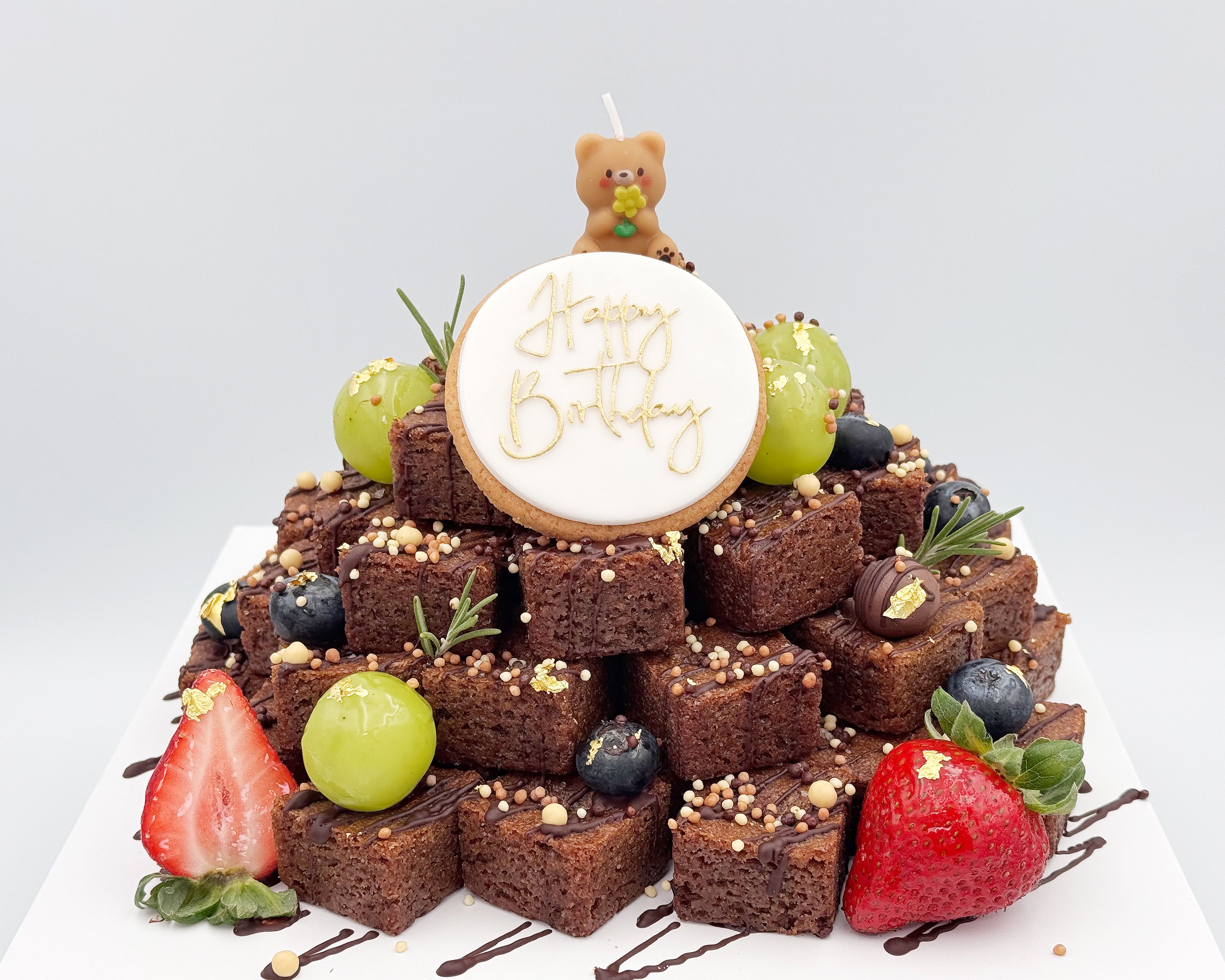 Brownie stacked cake with berries and a 'Happy Birthday' candle on a white background