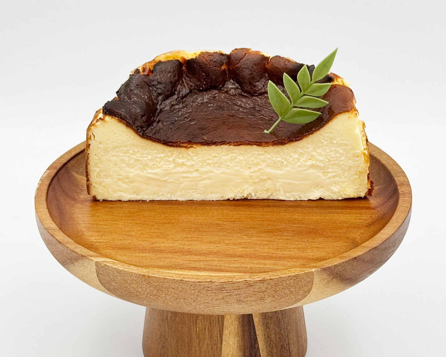 Cross-section of basque burnt cheesecake with a leaf on top, served on a wooden stand against a white background