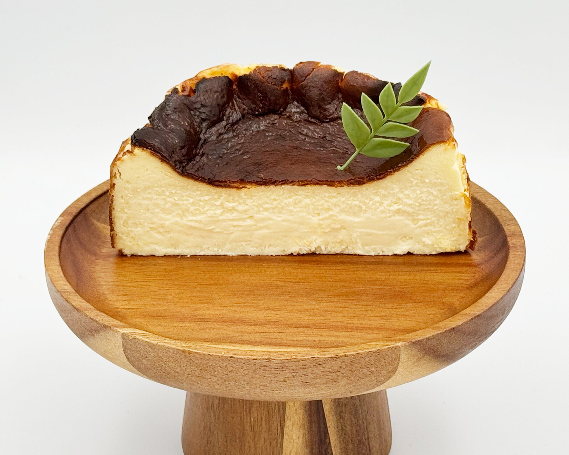 Cross-section of basque burnt cheesecake with a leaf on top, served on a wooden stand against a white background
