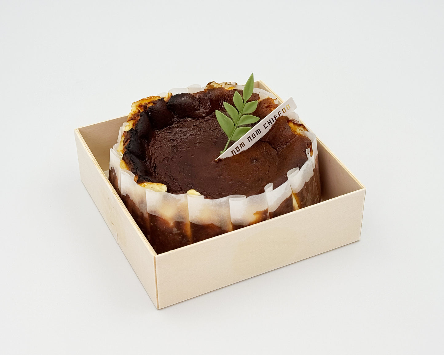 Basque burnt cheesecake in a box with a leaf decoration on a white background