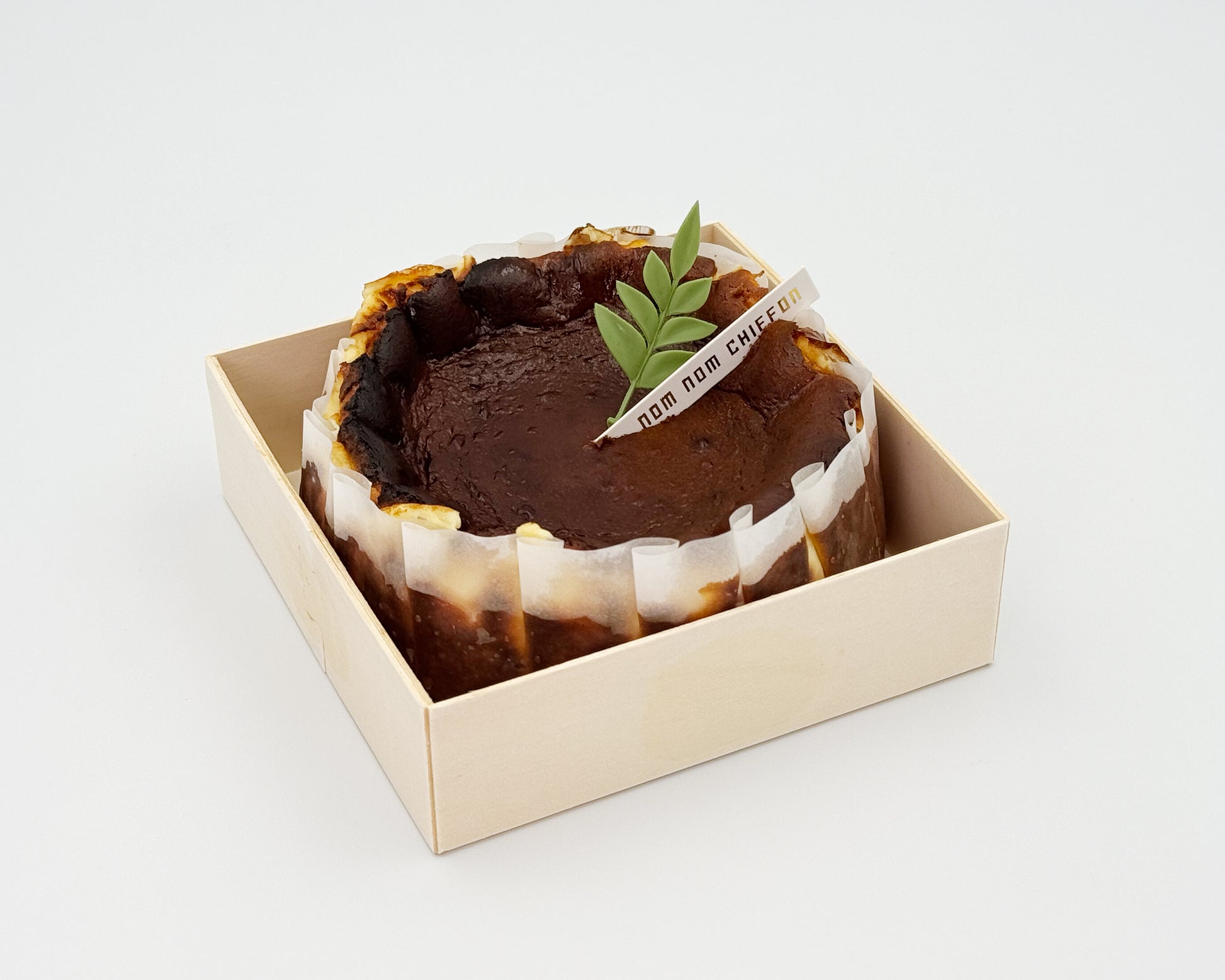 Basque burnt cheesecake in a box with a leaf decoration on a white background