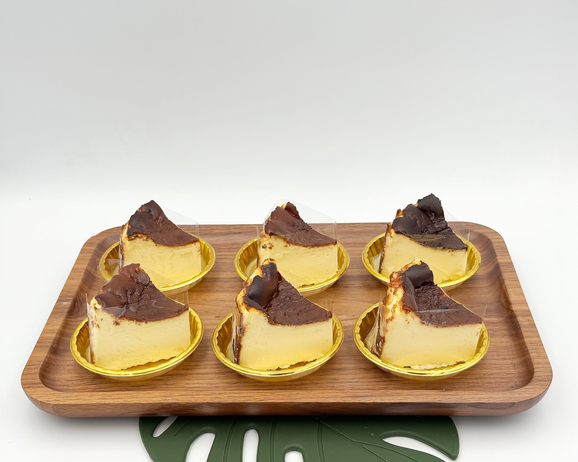 Six slices of basque burnt cheesecake arranged on a wooden tray against a white background.