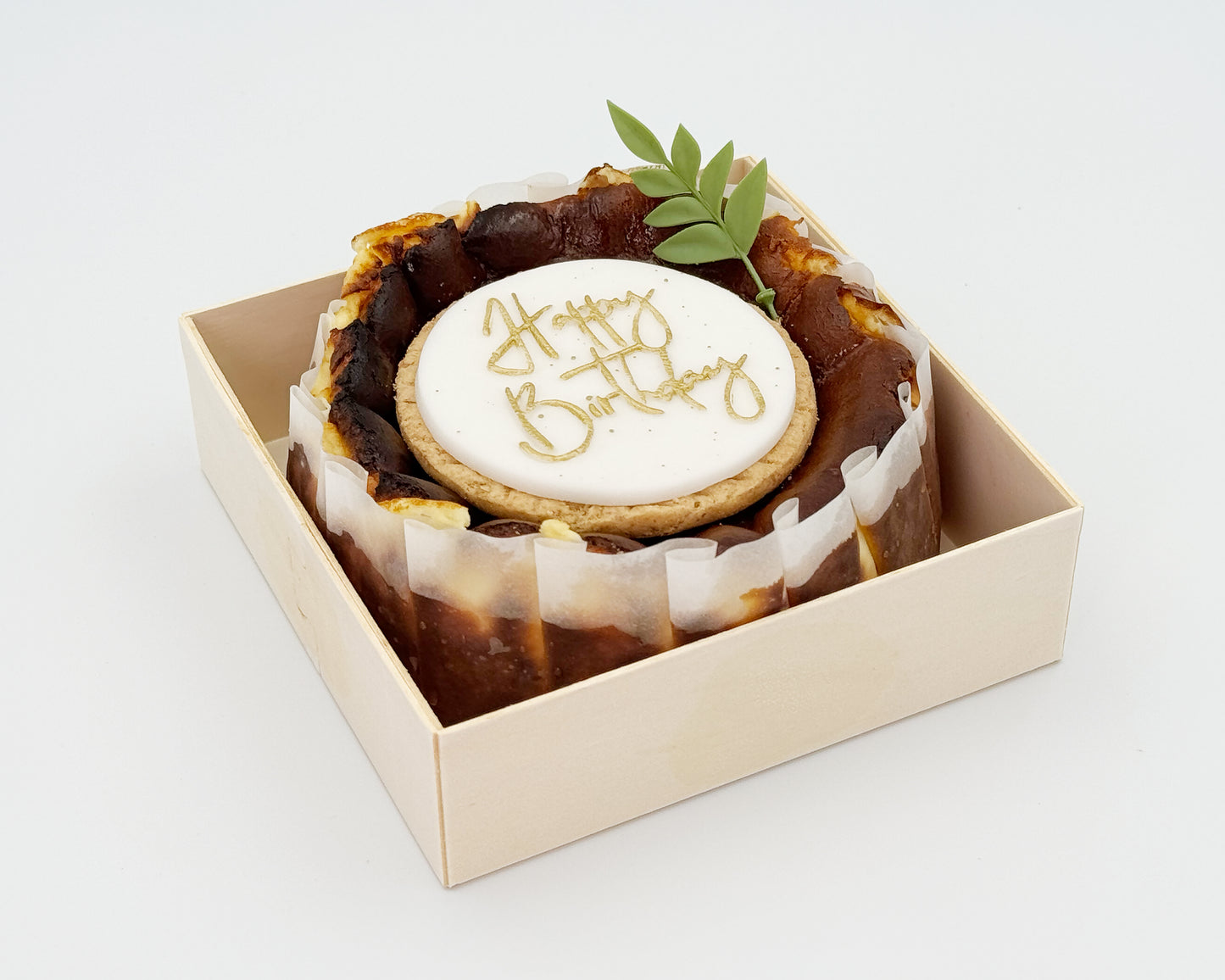Basque burnt cheesecake in a box with 'Happy Birthday' cake topper on a white background