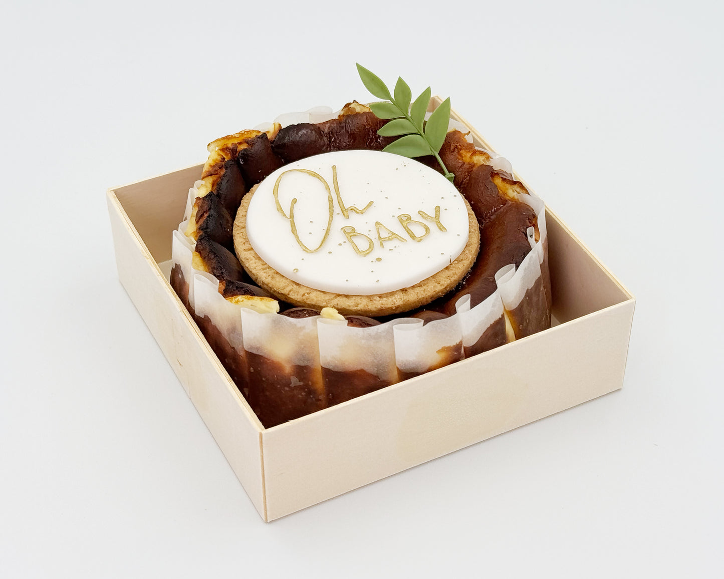 Basque burnt cheesecake in a box with 'Oh Baby' cake topper on a white background