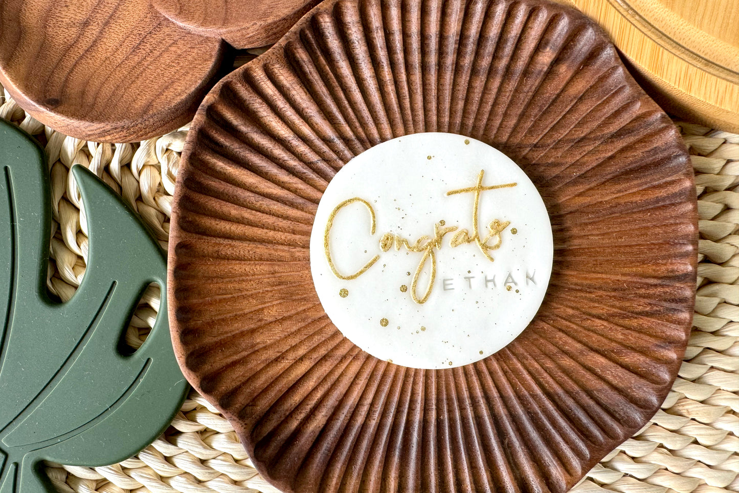 Wooden coaster with a white label reading 'Congrats Ethan' on a woven surface.