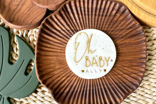 Wooden coaster with cake topper  'Oh Baby Ally' on a woven surface