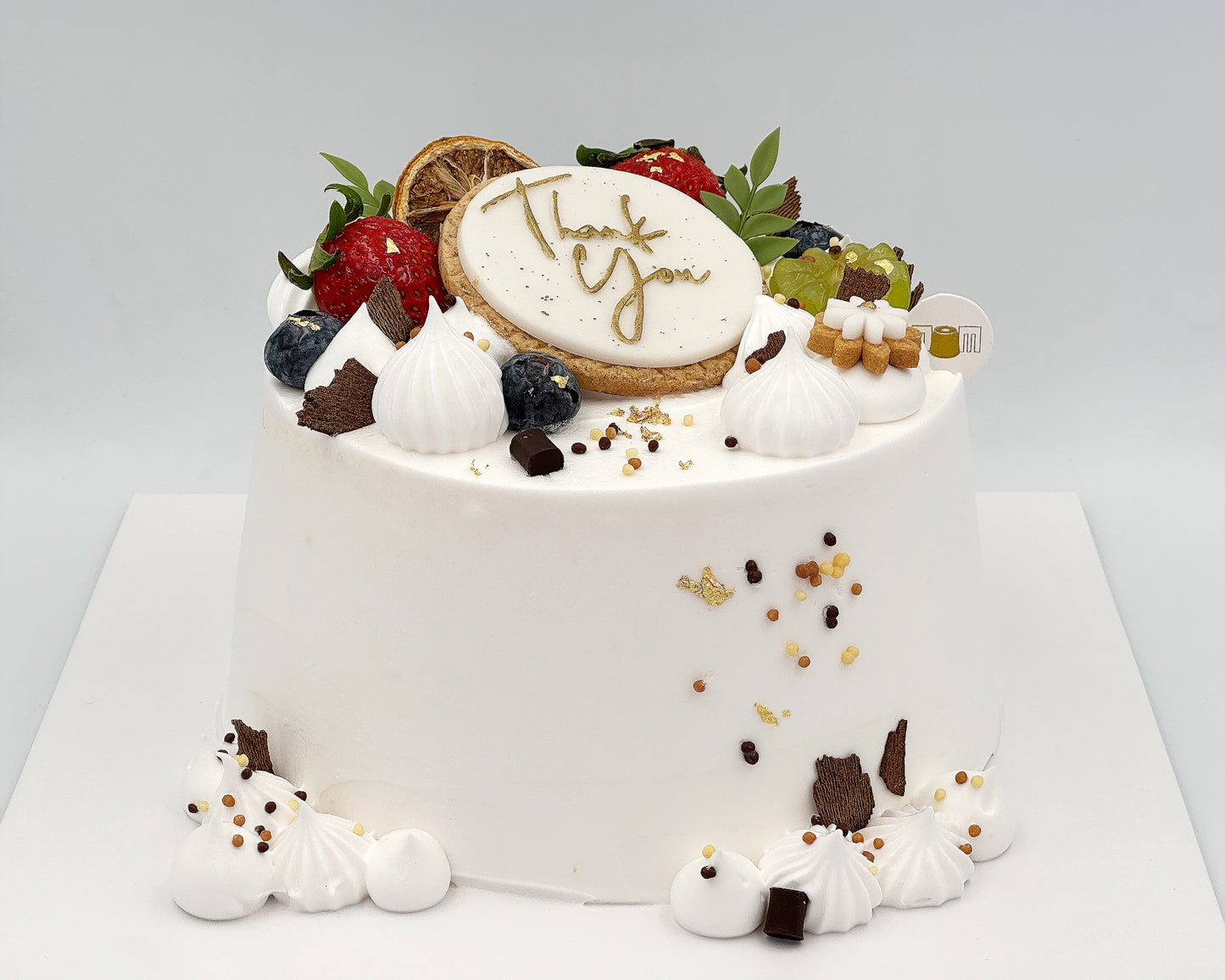 Decorative chiffon cake with fruits, cookies, and a decorative lettering on a white background