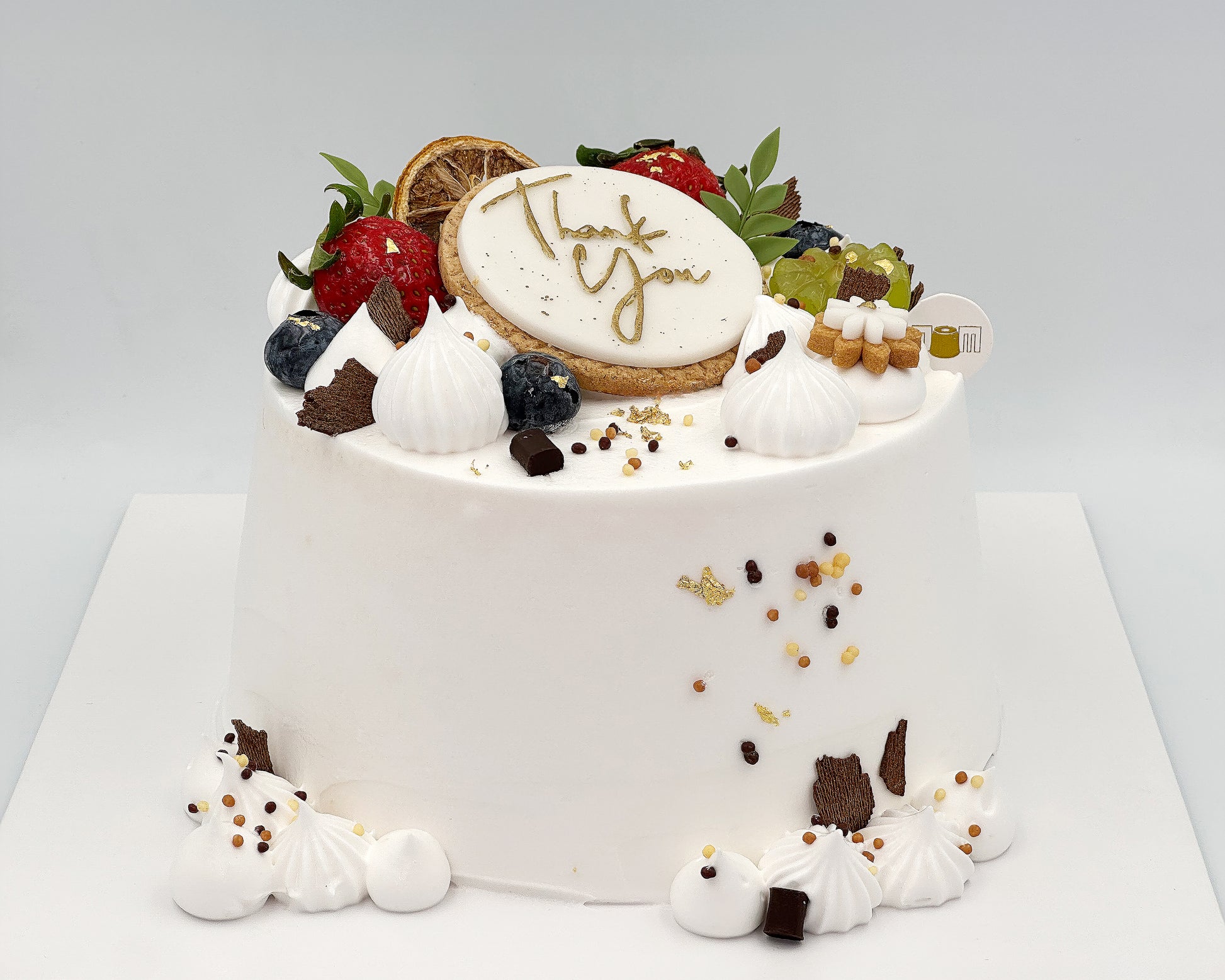 Decorative chiffon cake with fruits, cookies, and a decorative lettering on a white background