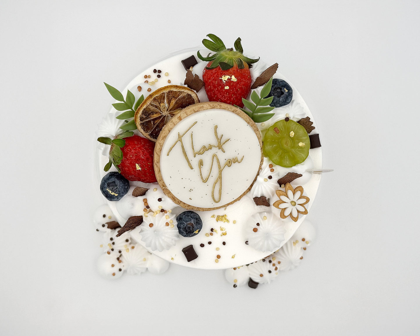 Top view of decorative chiffon cake with fruits and a cookie with 'Thank You' on a white background