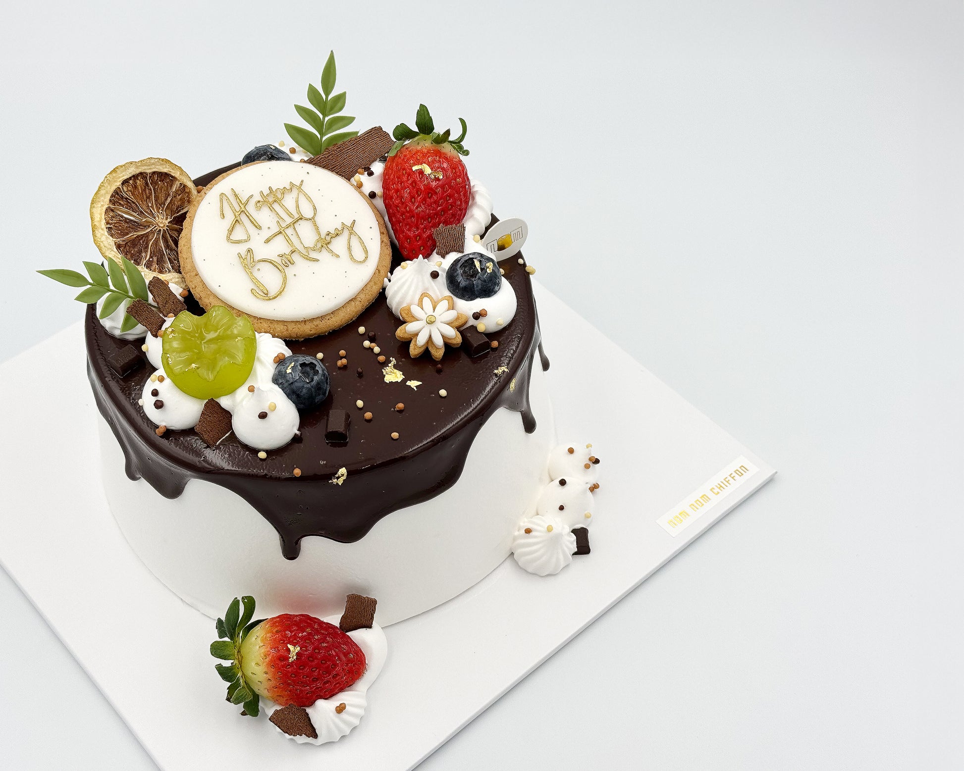 Decorative birthday cake with fruits and a cookie on a white background