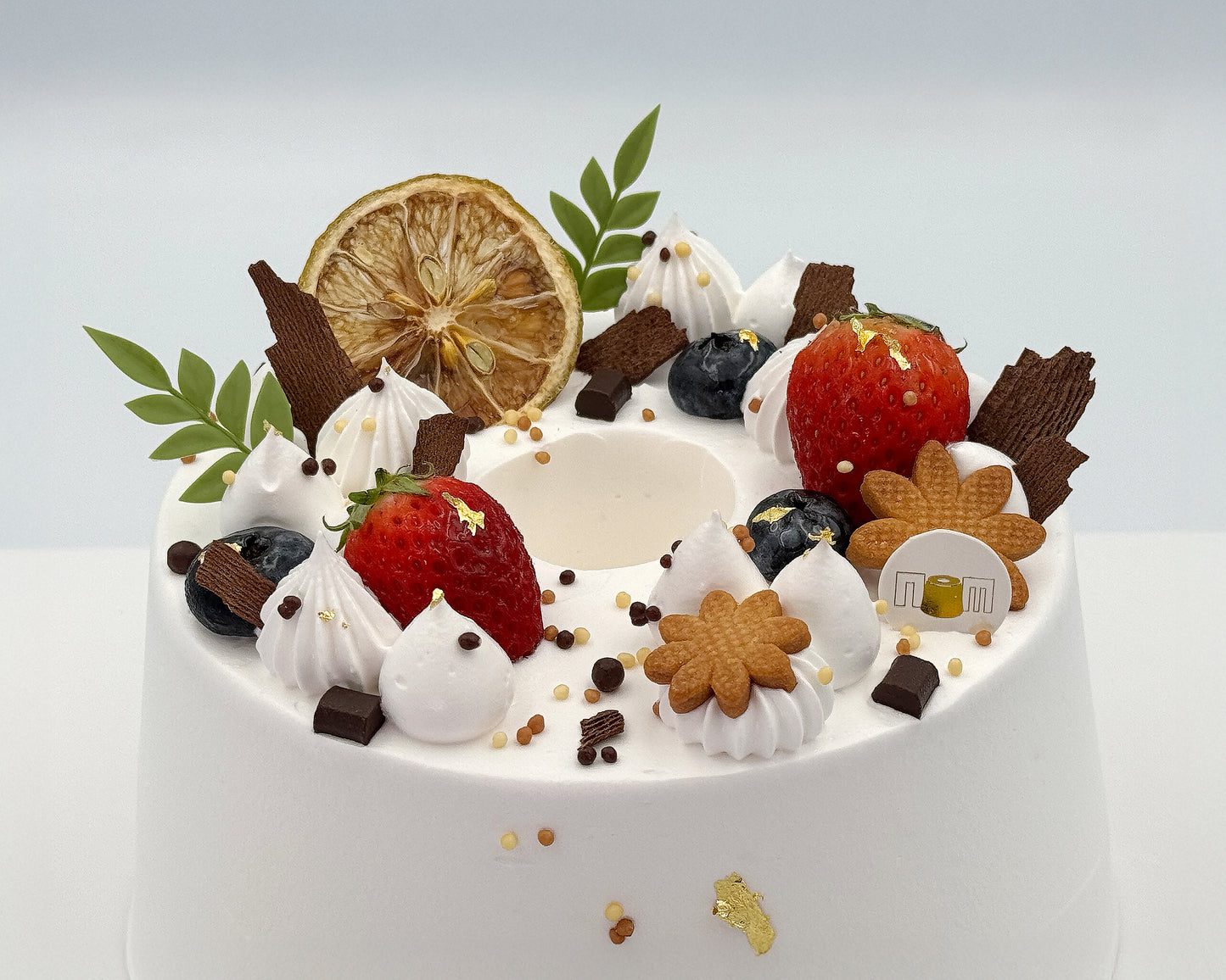 Close-up of decorative cake with fruits, cookies, and whipped cream on a light gray background