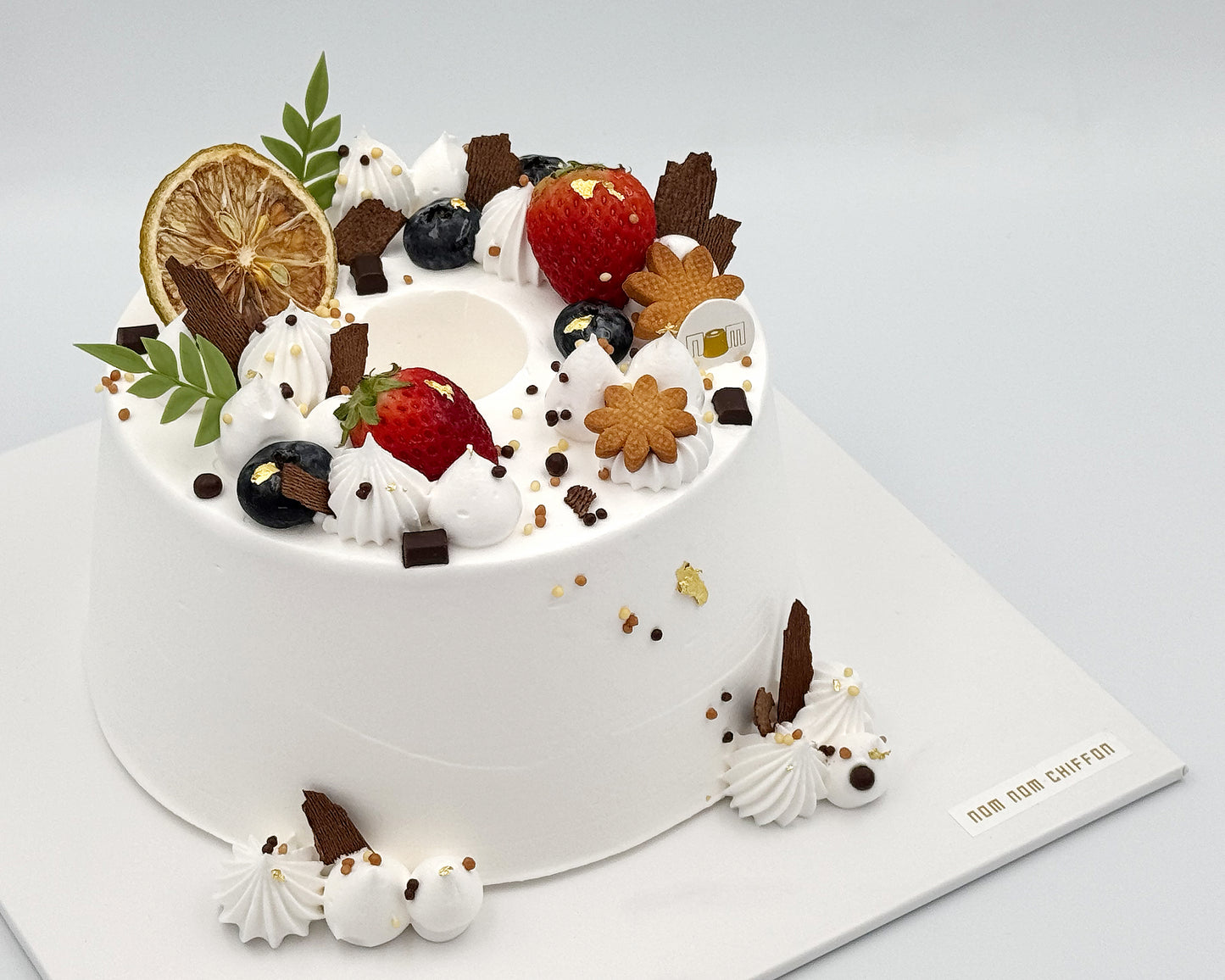 Decorative chiffon cake with fruits and cookies on a white background