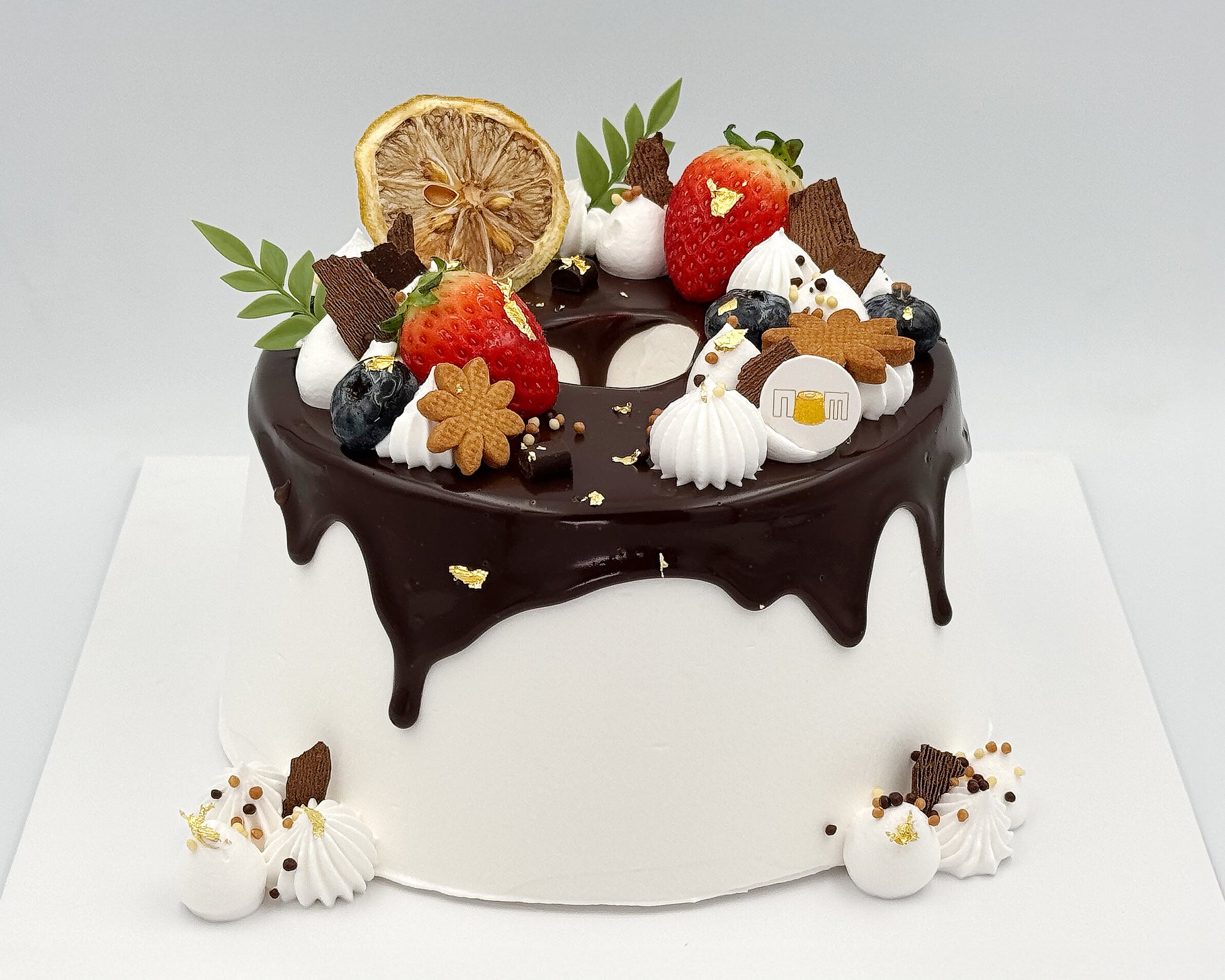Decorative cake with chocolate ganache, fruits, and cookies on a white background