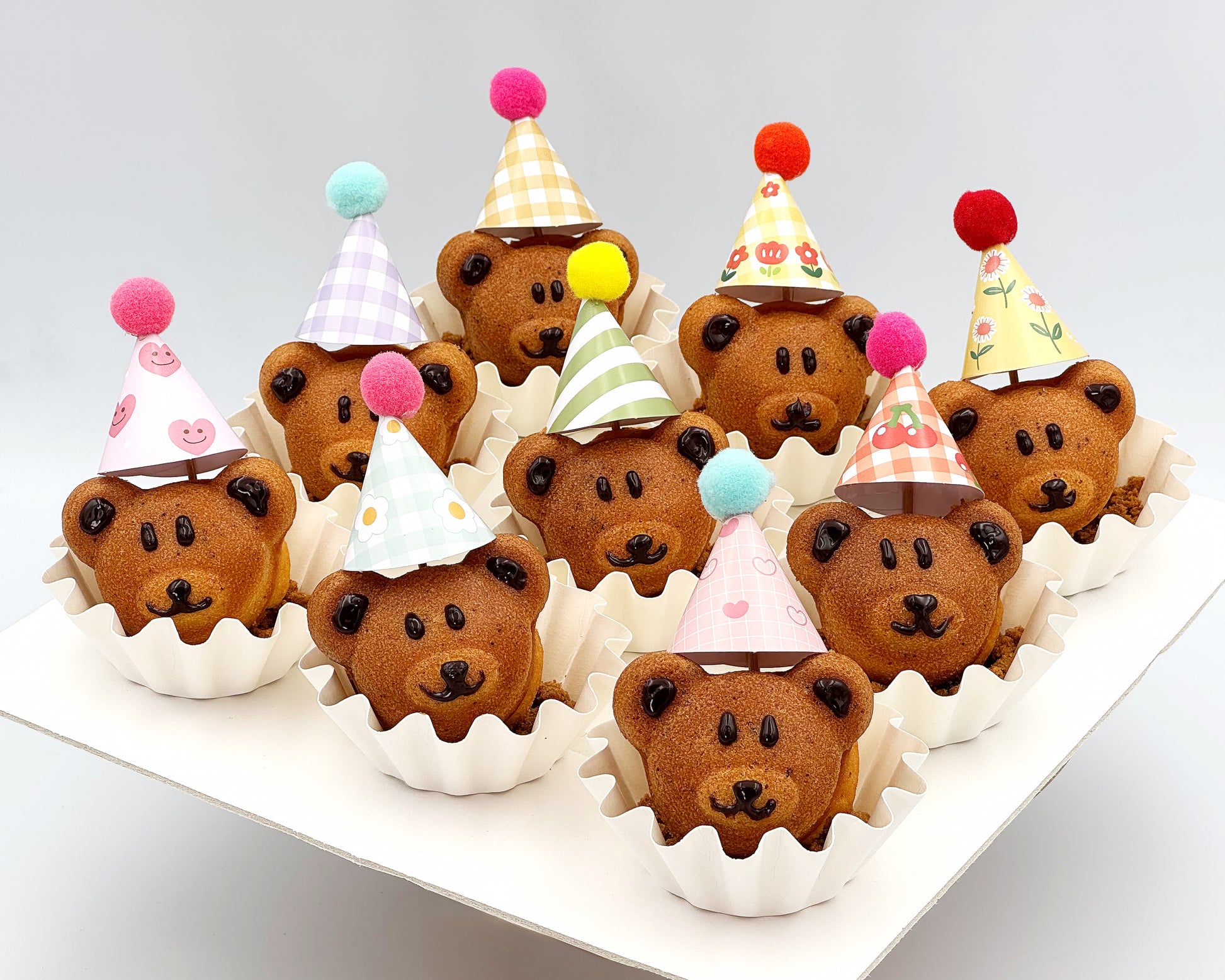 Bear-shaped madeleines with colorful party hats on a white surface