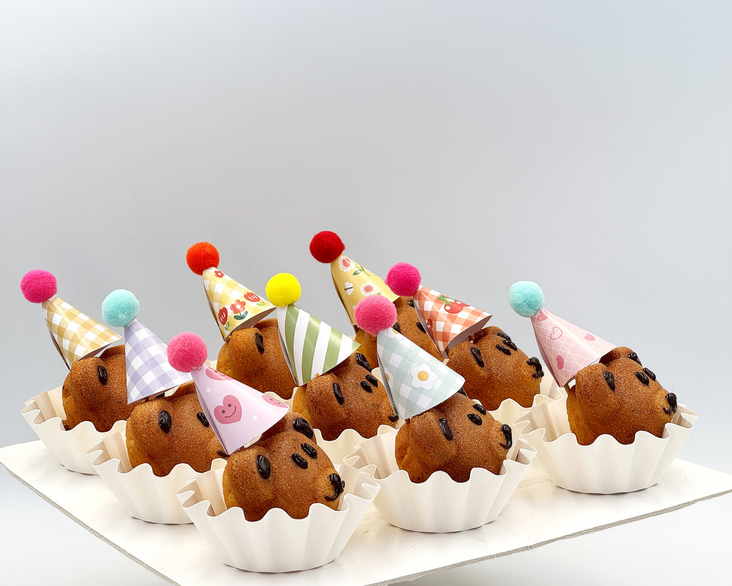 Side profile of bear madeleines with colorful party hats on a white surface.