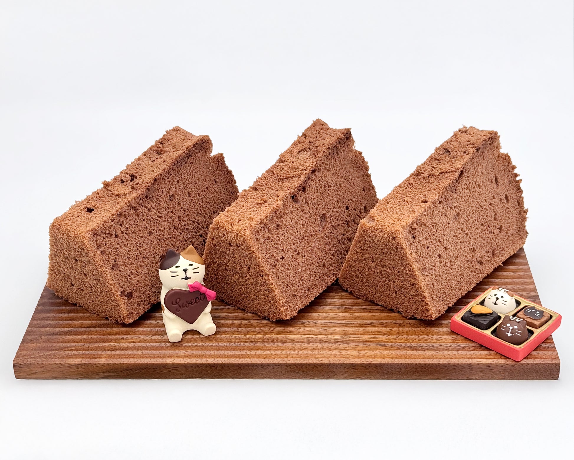 Three slices of chocolate chiffon cake on a wooden board with decorative items.