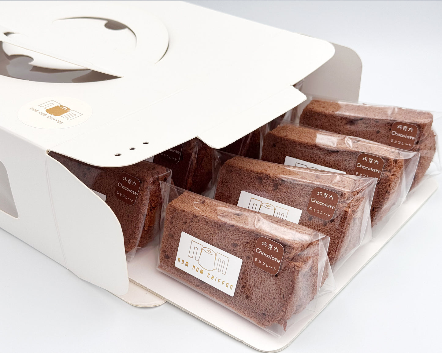 Packaged chocolate chiffon cake in clear plastic packaging with nom nom chiffon brand label on a white background.
