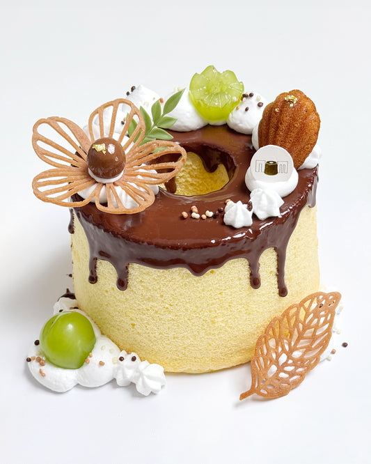Decorative cake with chocolate ganache, flower tuile, mini madeleines, cookies, and fruits on a white background
