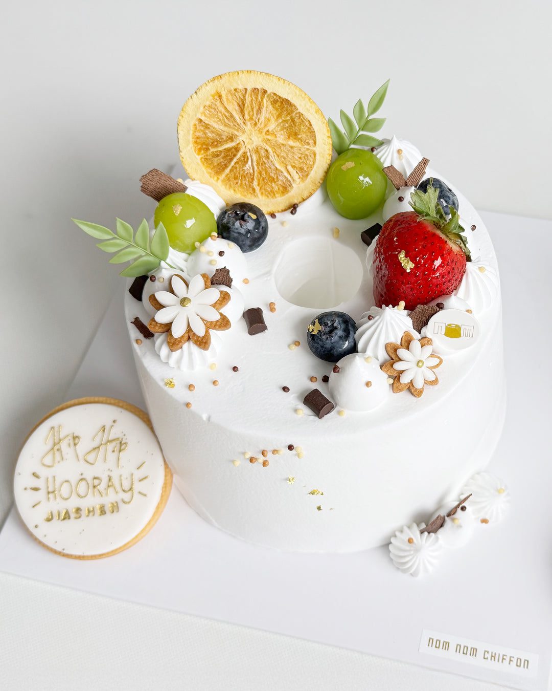 Decorative cake with fruits and a 'Hip Hip Hooray' cake topper cookie on a white background